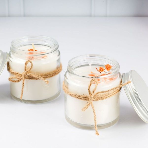 Two soy candles in glass jars tied with twine and topped with dried orange flowers