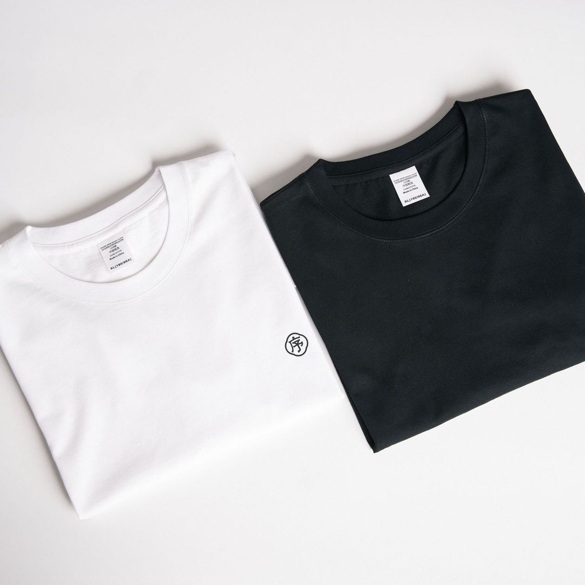 A white and a black crew-neck t-shirt folded side by side on a plain background