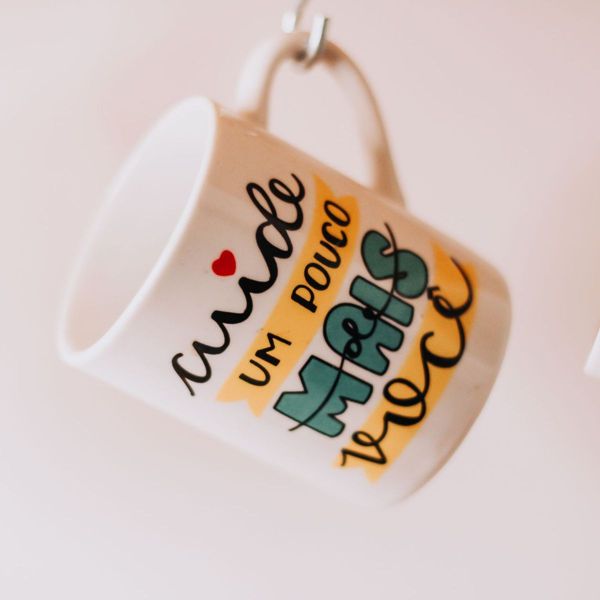 White ceramic mug with colourful hand-lettered text hanging from a hook